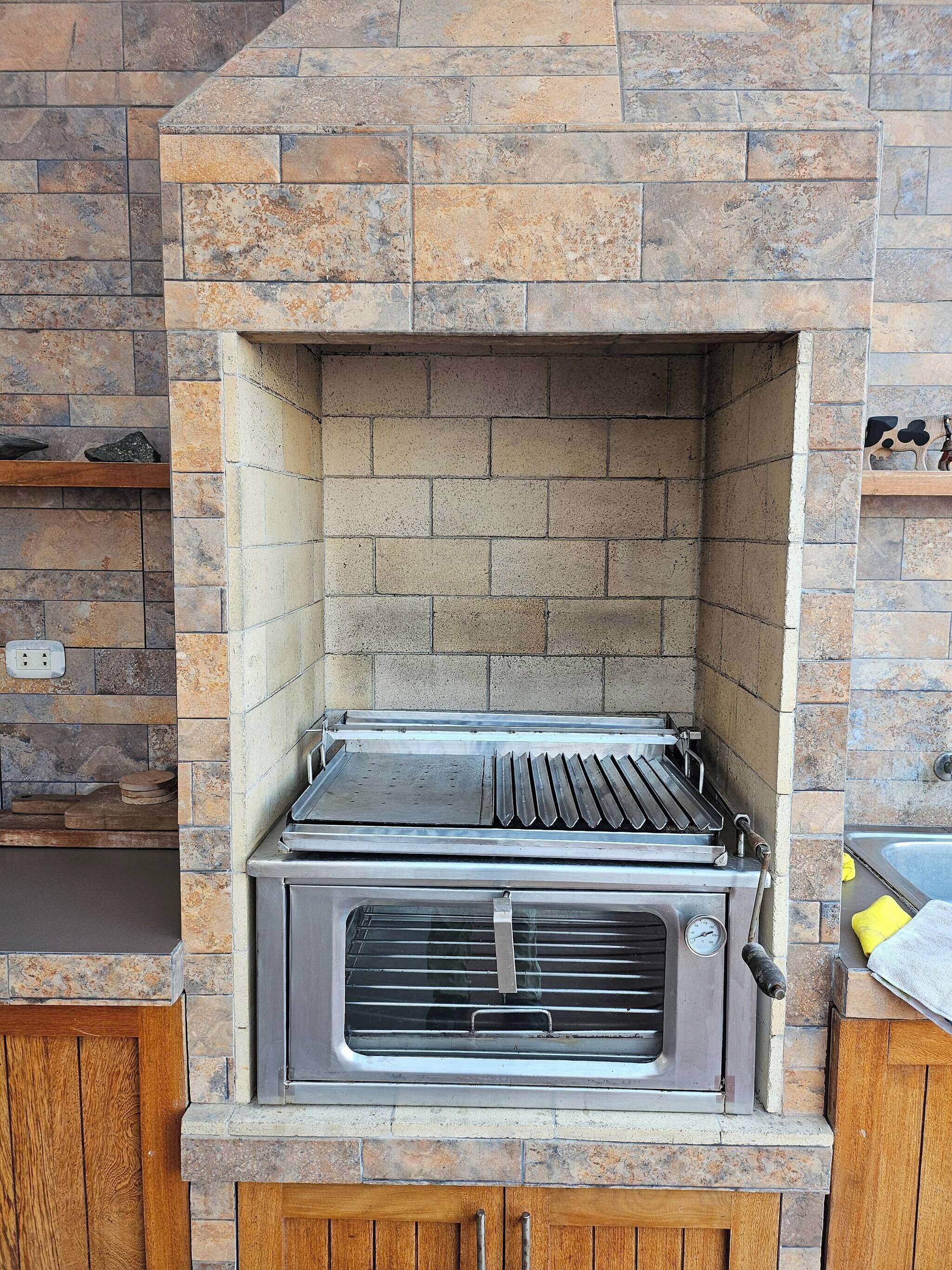 A brick-built outdoor grill with a metal grate and control panel, surrounded by stone walls.