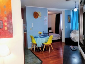 Un espacio habitable compacto con comedor que incluye una mesa, sillas, cama, ventilador y un teléfono montado en la pared.