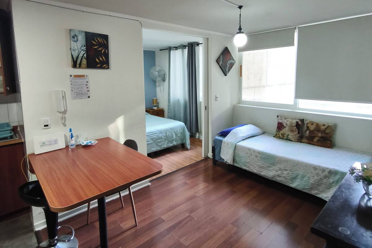 Een compacte kamer met houten vloer, een eettafeltje, een bank en een bed.