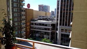 Een balkon met een bloempot, met uitzicht op een stadsgezicht met meerdere hoge gebouwen en een heldere lucht.