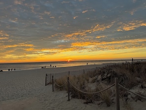 A beach with a wooden fence and rope barrier, sandy beach, and a sunset over the ocean. - Bright condo-On bike trail & 1 mile to boardwalk (Rehoboth Beach)