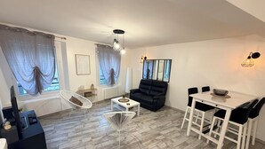 A modern living room with a black sofa, white chairs, a dining table, and a TV stand. - House in the heart of Sisteron (Sisteron)