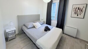 A modern bedroom with a bed, bedside tables, a window with curtains, a radiator, and a wall-mounted artwork. - House in the heart of Sisteron (Sisteron)