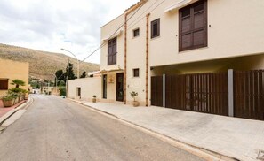 Una vista di strada con un edificio dotato di ingresso recintato, un piccolo portico e una montagna sullo sfondo.