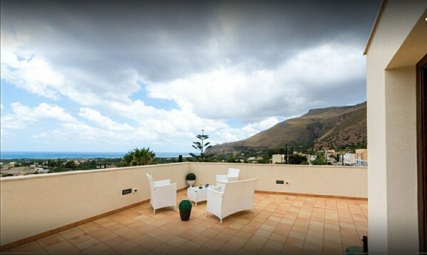 A terrace with white chairs and a table, overlooking a coastal landscape with mountains and a view of the sea. - Beb Coppola  (Castelluzzo)