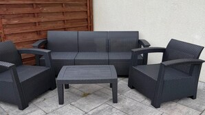 Un ensemble de mobilier d’extérieur en osier, comprenant un canapé, deux fauteuils et une petite table.