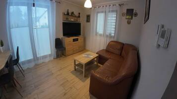 Una sala de estar con un sofá de cuero marrón, una mesa de centro de madera, un televisor sobre un mueble de madera, y un comedor con mesa y sillas.