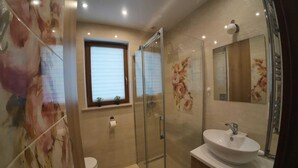 Une salle de bain avec une douche à parois de verre, des toilettes, un lavabo et une fenêtre avec des stores.