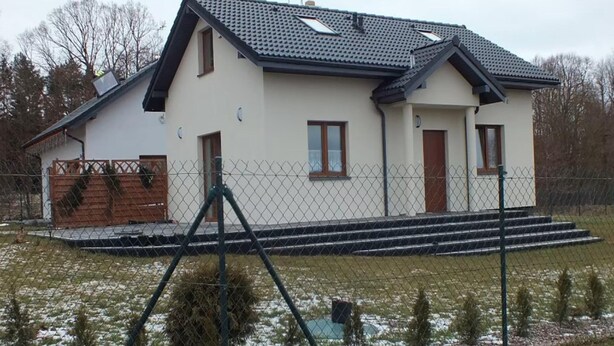 Une maison à deux étages avec un toit en pente, une cour clôturée et un petit escalier menant à l’entrée.
