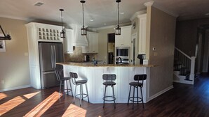 A kitchen with a central island, bar stools, a refrigerator, and pendant lighting. - On The Pond (Granbury)