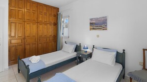 A bedroom with two single beds, wooden wardrobes, a nightstand with a lamp, and a painting on the wall. - Anthoula's Sea View Apartment (27R5+C6 Piso Livadi)