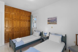 A bedroom with two single beds, wooden wardrobes, a nightstand with a lamp, and a painting on the wall. - Anthoula's Sea View Apartment (27R5+C6 Piso Livadi)
