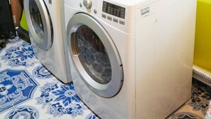 Pesutila, jossa on kaksi pesukonetta, pieni hylly puhdistusaineille ja kuvioitu lattia.