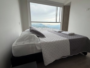 Una cama individual con colcha blanca y gris, una almohada y una manta.