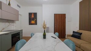 A modern kitchen with a marble countertop, a built-in oven, and a dining area with a marble table and blue chairs. - LUXURY BERGAMO CITY APARTMENTS champagnerie (Bergamo)
