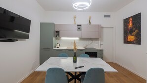 A modern kitchen with a flat-screen TV, a dining table with chairs, and a painting on the wall. - LUXURY BERGAMO CITY APARTMENTS champagnerie (Bergamo)
