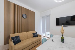 Ein modernes Wohnzimmer mit einer Couch, einem Tisch, einer Vase und einem an der Wand befestigten Fernseher.