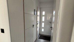 Un couloir étroit aux murs blancs, doté d’un sol carrelé et d’une porte au fond.