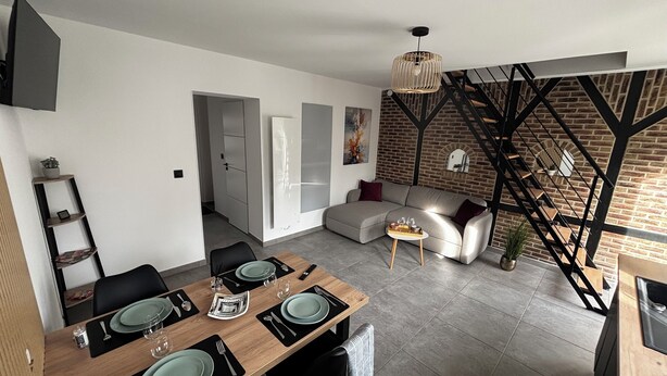 Un espace de vie moderne comprenant un coin repas, un canapé et un escalier adossé à un mur de briques.