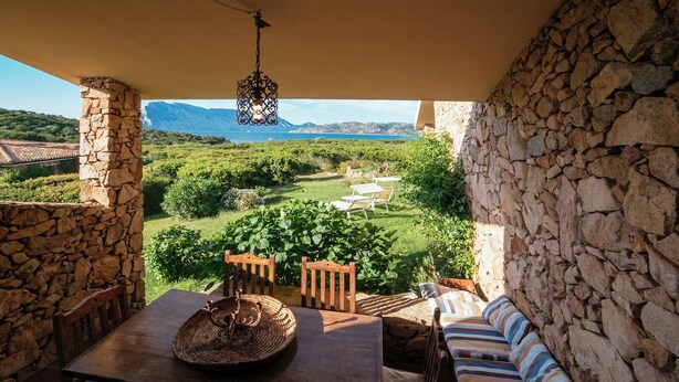 Una habitación con paredes de piedra y vistas a un jardín exuberante y montañas.