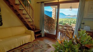Un salón acogedor con una escalera de madera, un sofá amarillo, una alfombra estampada y vistas a montañas a través de un ventanal.