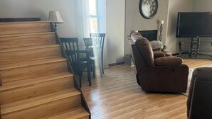Un salon avec un escalier en bois, un canapé en cuir marron, une table à manger avec des chaises, un téléviseur à écran plat et une cheminée.