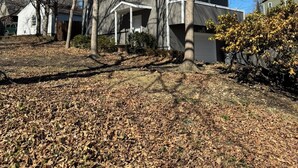 Un bâtiment à deux étages avec un garage, entouré d’un sol couvert de feuilles et d’arbres sans feuilles.