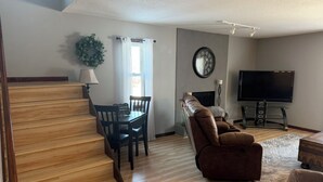 Un salon moderne avec un escalier, un coin repas, un canapé, un téléviseur et une cheminée.