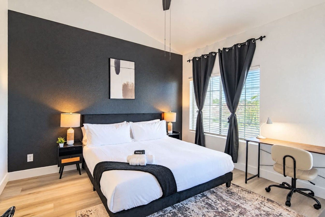 A modern bedroom with a large bed, bedside lamps, a desk, and a chair.