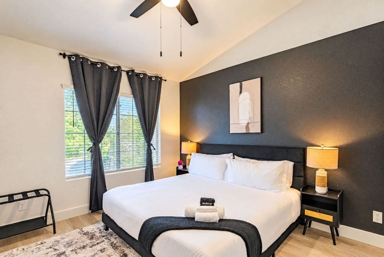 A modern bedroom with a large bed, a ceiling fan, a bedside table with a lamp, and a window with curtains.