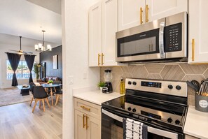 A modern kitchen with stainless steel appliances, a dining area with a table and chairs, and a view of the outdoors through large windows. - Stylish Getaway | Pool, Spa & Relaxing Balcony (Scottsdale)