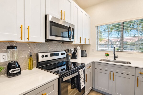 A modern kitchen with white cabinets, a stainless steel microwave, a black stove, and a window with a view of houses.