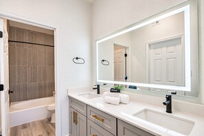 A modern bathroom with a large mirror, two sinks, a toilet, and a shower area.