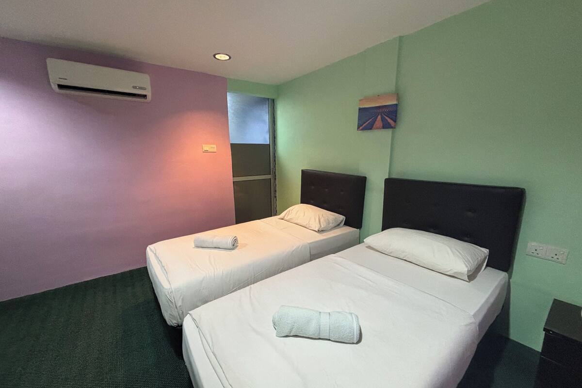 Hotellihuone, jossa on kaksi erillistä sänkyä, ikkuna, ilmastointilaite ja pieni taulu seinällä.