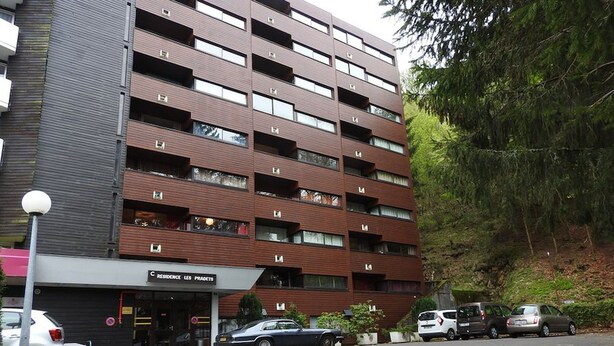 Un edificio de varios pisos con diseño moderno, que cuenta con una entrada a nivel de calle con un cartel y varios coches estacionados frente a él.