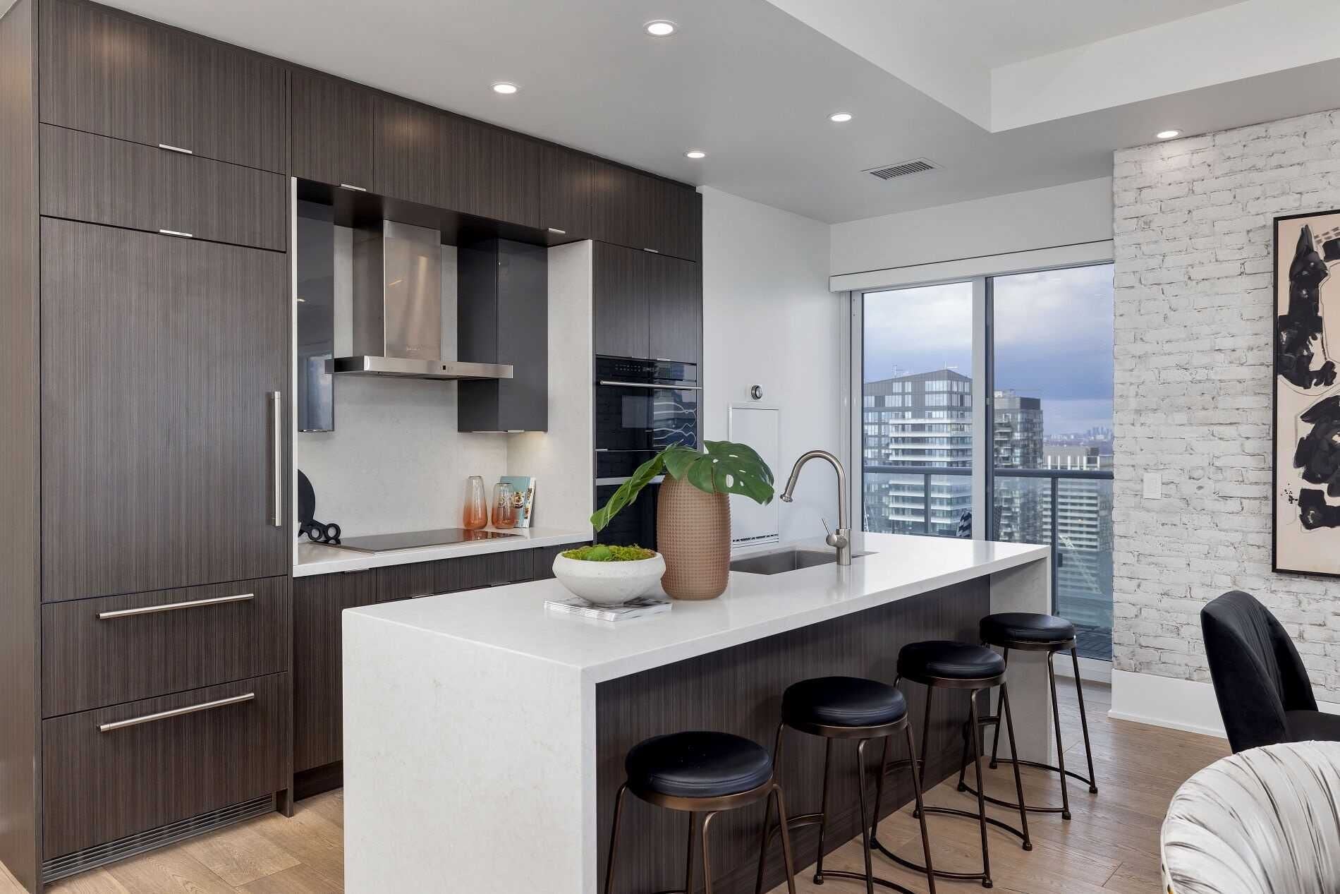 Una cocina moderna con alacenas de madera oscura, encimera blanca y un amplio ventanal con vista a la ciudad.