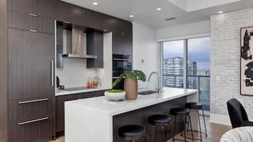 Una cocina moderna con alacenas de madera oscura, encimera blanca y un amplio ventanal con vista a la ciudad.