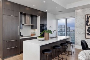 A modern kitchen with dark wood cabinets, a white countertop, and a large window offering a city view. - Aera Toronto - The Entertainment District (Toronto)