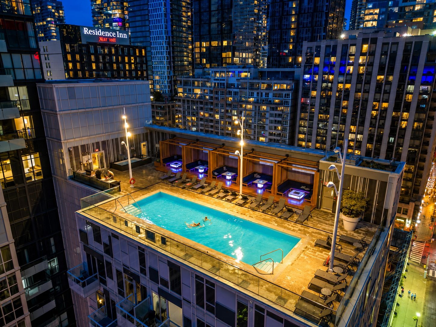 A rooftop pool area with lounge seating and a view of the city skyline at night.