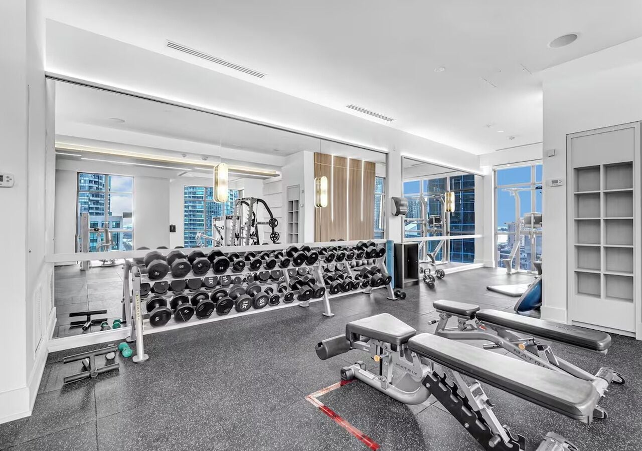 Une salle de sport moderne équipée de matériel de musculation, de tapis de course et d’un mur rempli de haltères.