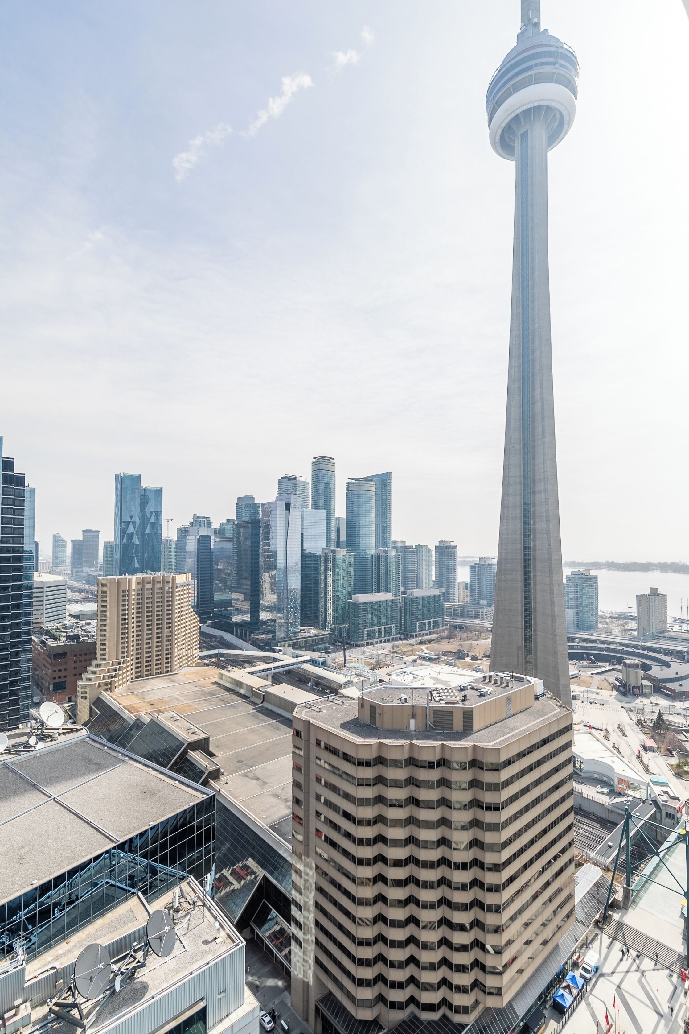 A high-rise building with a distinctive tower, surrounded by modern skyscrapers and a body of water in the background.