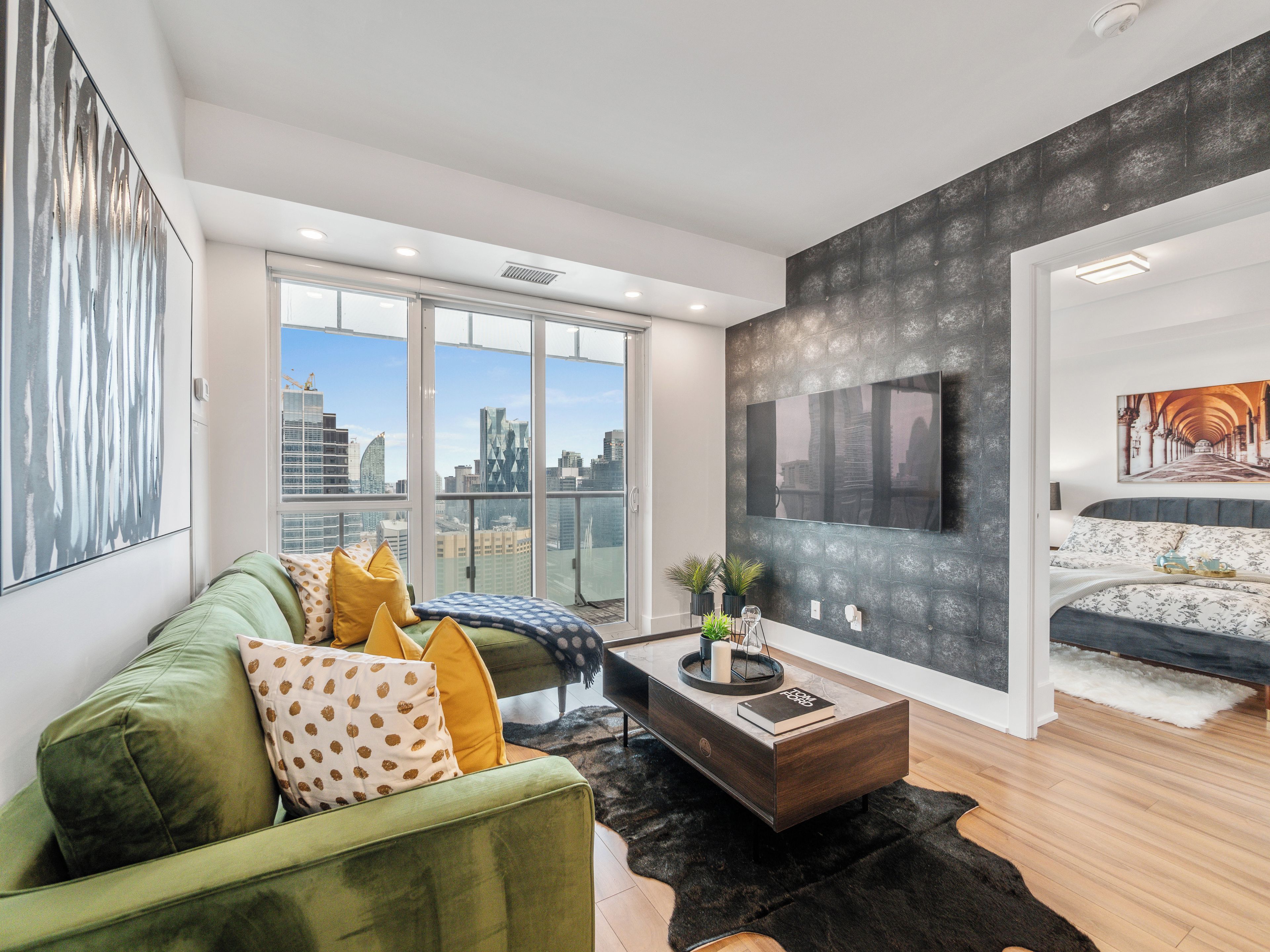 A modern living room with a green sofa, a coffee table, and a city view through large windows.