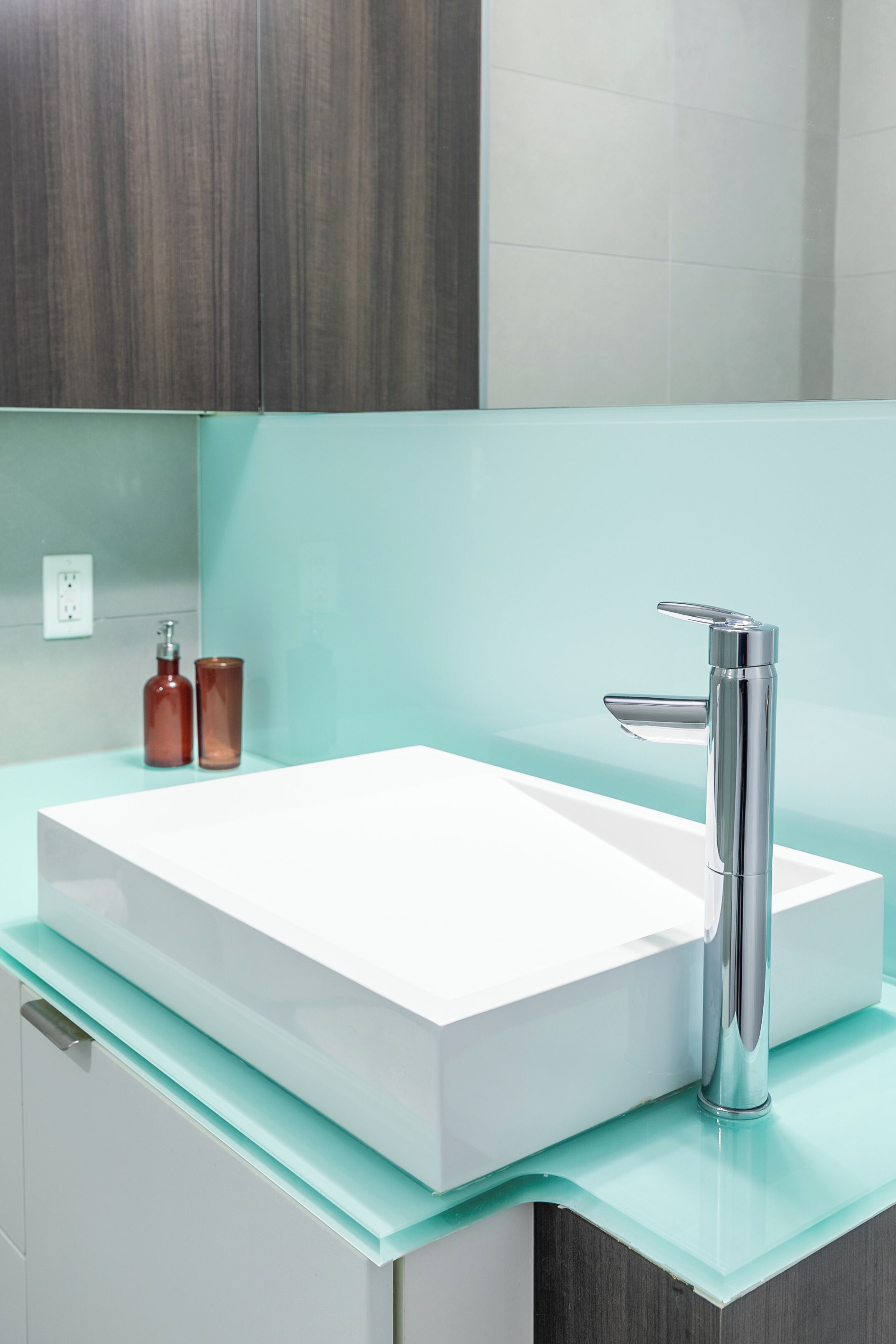 Un baño moderno con lavamanos blanco, grifo cromado y encimera de cristal.