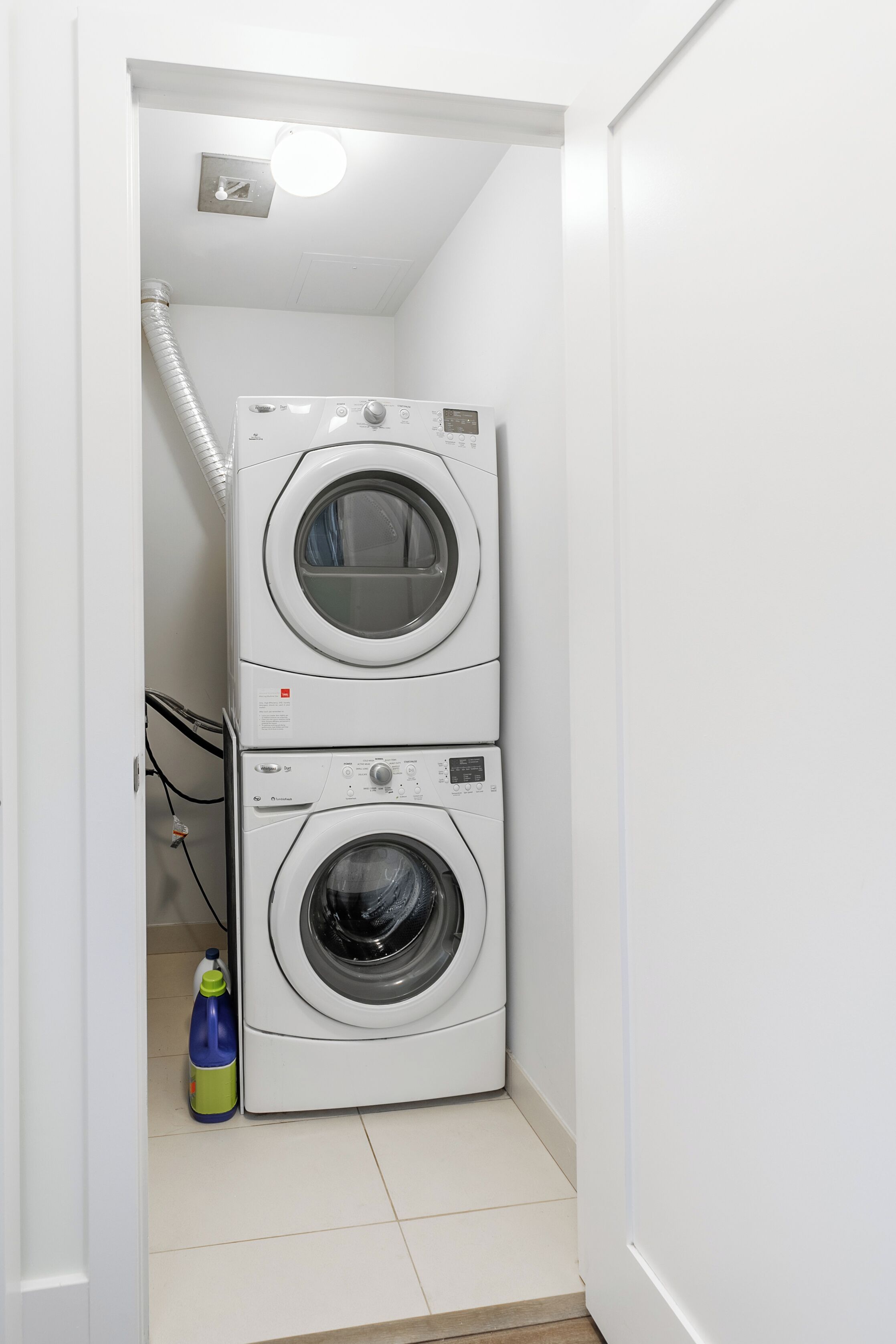 A laundry room with two stacked front-loading washing machines and a detergent bottle on the floor.
