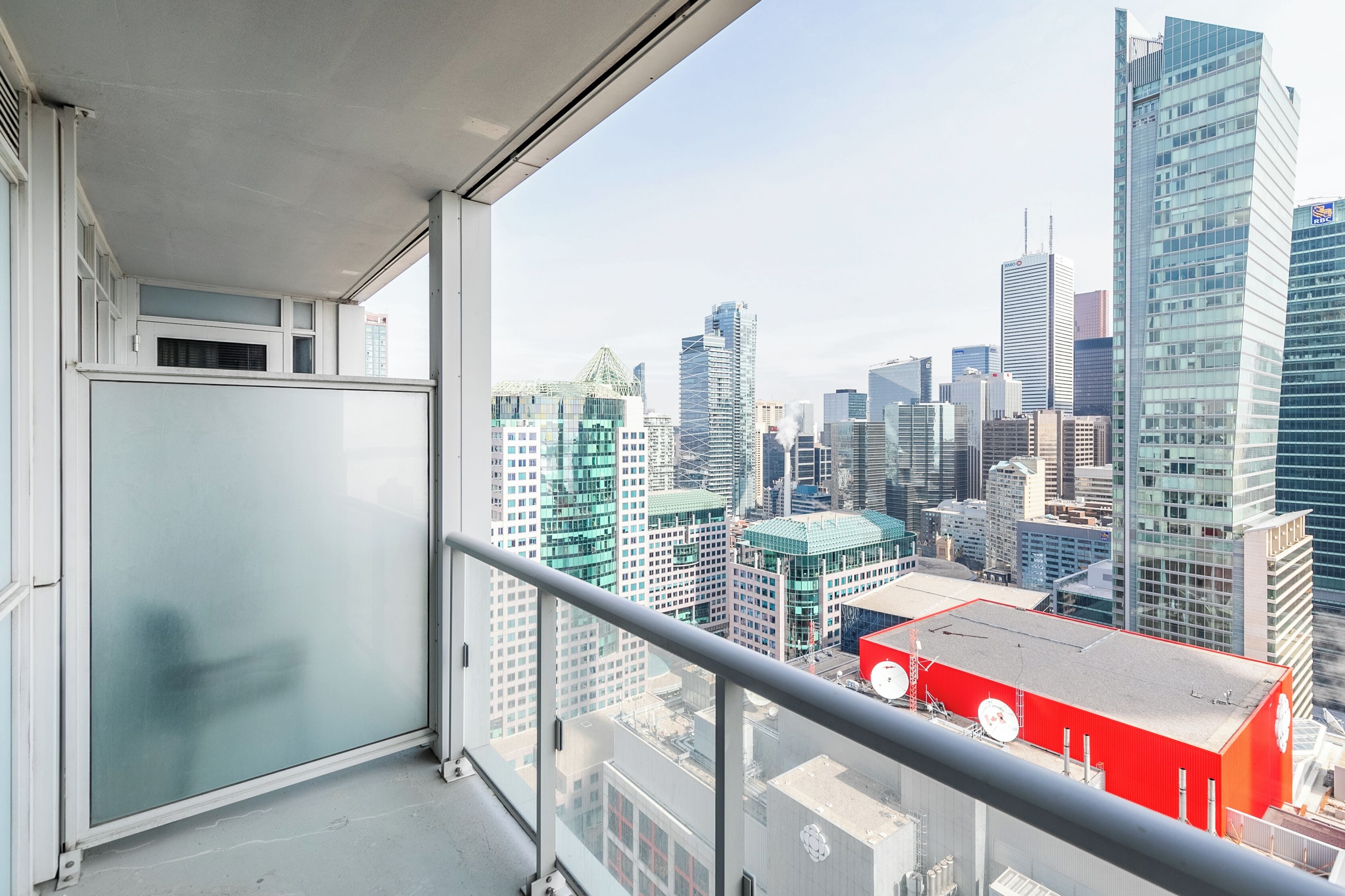 A high-rise building with a view of a cityscape through a balcony with a glass door and a metal railing.