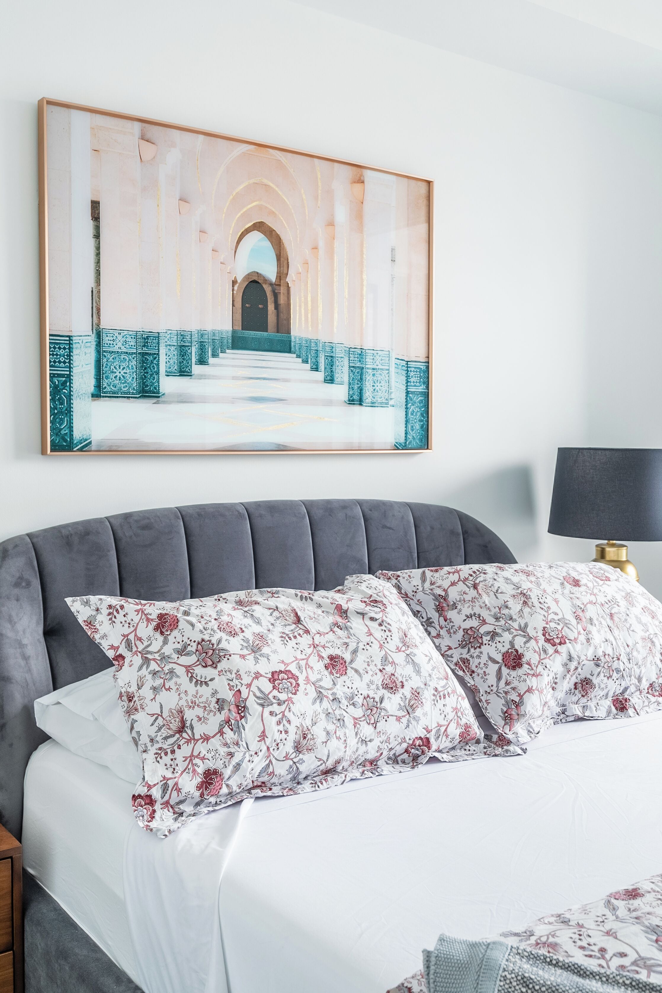 Un dormitorio con una cama grande, una obra enmarcada sobre ella y una mesita de noche con una lámpara.