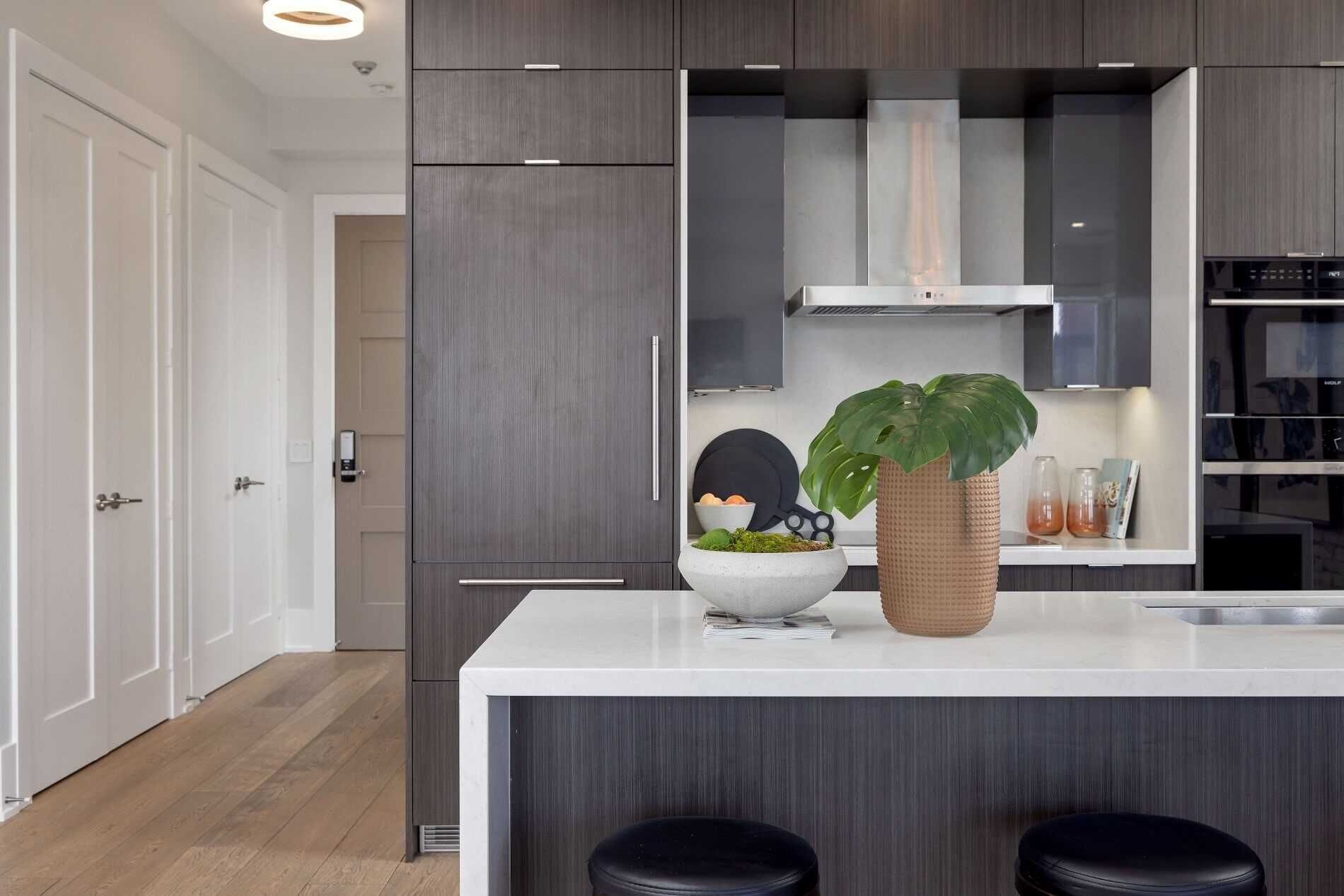 A modern kitchen with dark wood cabinets, a white countertop, and a central island with stools.