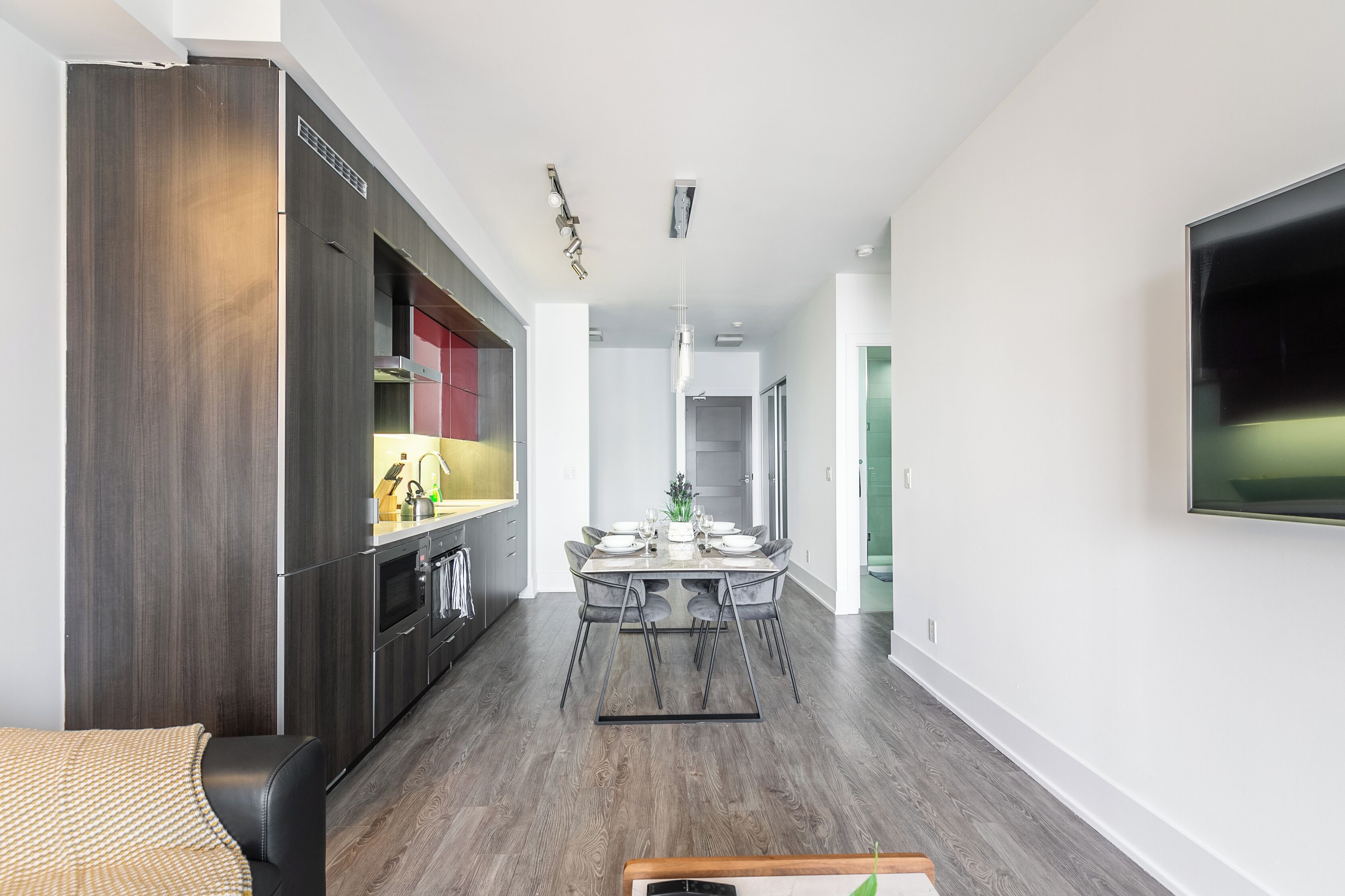 Une cuisine moderne avec des meubles en bois foncé, un coin repas doté d’une table en marbre et un téléviseur à écran plat fixé au mur.