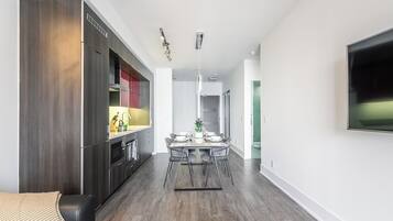 Une cuisine moderne avec des meubles en bois foncé, un coin repas doté d’une table en marbre et un téléviseur à écran plat fixé au mur.