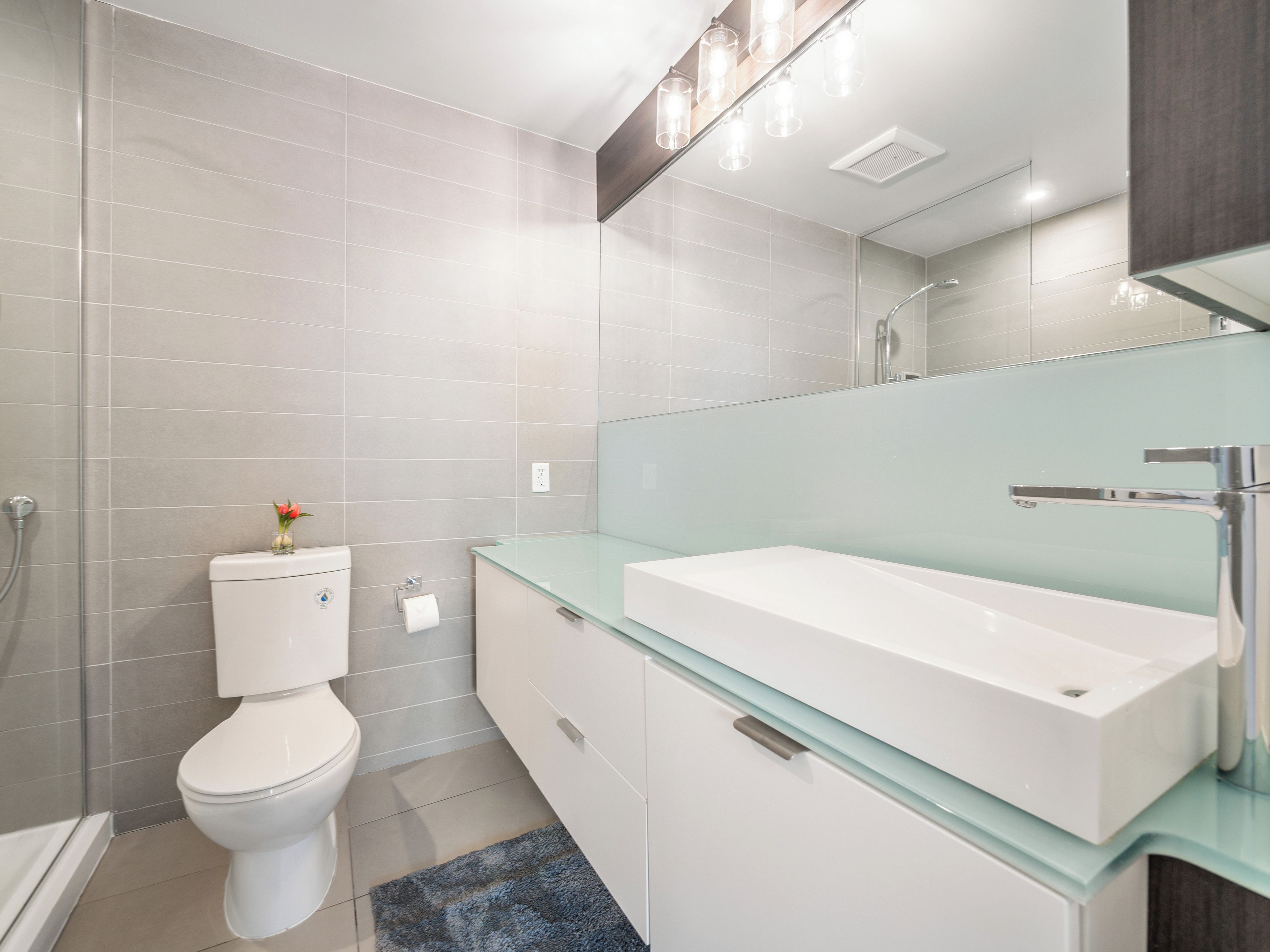 Une salle de bain moderne avec un meuble-lavabo en verre, des toilettes et une douche.